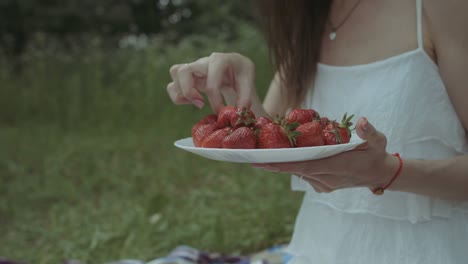 Joyful-woman-eating-strawberry-on-picnic