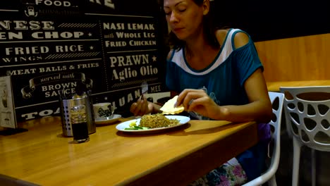 A-woman-in-a-restaurant-at-the-table-eats-nasi-goreng-and-pours-its-soy-sauce