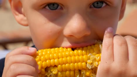 Niño-hambriento-comiendo-maíz-en-la-playa-del-mar.-Se-centran-en-el-maíz-hervido.-Close-up.