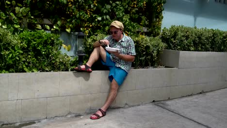 Comida-en-la-calle.-Un-hombre-sentado-en-la-calle-a-un-parapeto-comer-verduras-guisadas-de-un-recipiente