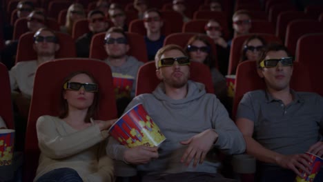 Young-people-sitting-in-movie-theater-watching-3D-movie-and-eating-popcorn