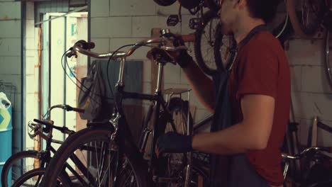 theme-small-business-bike-repair.-A-young-Caucasian-brunette-man-wearing-safety-goggles,-gloves-and-an-apron-uses-a-hand-tool-to-repair-and-adjust-the-bike-in-the-workshop-garage