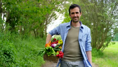 Portrait-of-a-happy-young-farmer-holding-fresh-vegetables-in-a-basket.-On-a-background-of-nature.