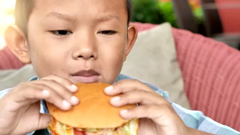 Niedlichen-asiatischen-jungen-freuen-uns-einen-Hamburger-Essen-im-Restaurant.-4k-Video-Zeitlupe