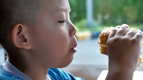 Cerca-niño-asiáticos-comer-hamburguesa,-lindo-muchacho-feliz-con-hamburguesa-en-el-restaurante.-Video-Slow-motion