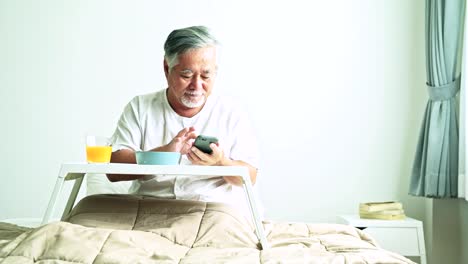 Senior-man-using-mobile-to-call-nurse-to-collect-his-finished-breakfast.-Beautiful-asian-woman-with-old-asian-man-with-white-beard-in-bed.-Senior-home-service-concept.