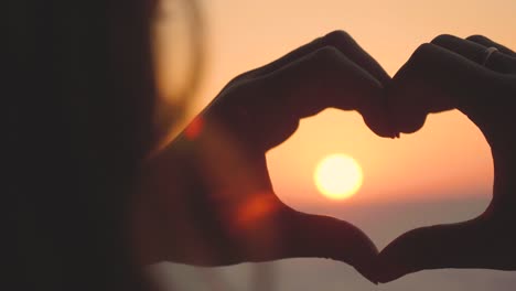 Portrait-of-a-young-girl-at-the-sea,-making-a-heart-shape-with-her-hands,-beach-background.