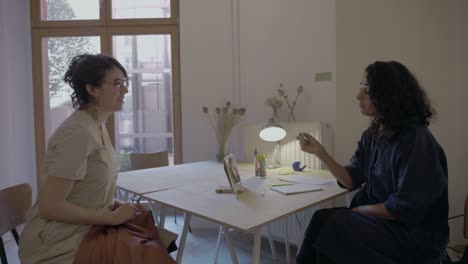 Two-business-women-have-a-meeting-or-job-interview-together-with-electronic-device-on-a-casual-and-friendly-meeting