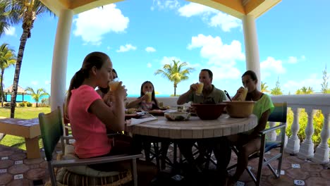 Caucasian-family-dining-on-vacation-beach-hotel-decking