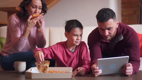 Familie-mit-Hilfe-von-digital-Tablette-während-des-Essens-Pizza-im-Wohnzimmer