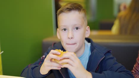 Junger-Teenager-essen-leckere-Hamburger-im-Fastfood-Restaurant.