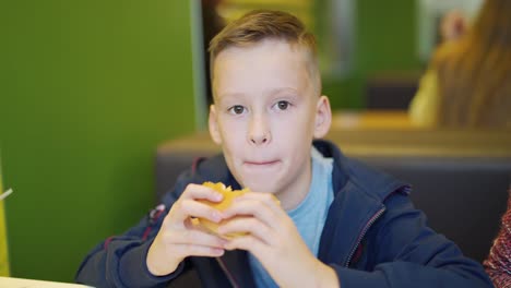 Young-teenager-eating-tasty-hamburger-in-fast-food-restaurant.