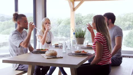 Four-young-adult-friends-celebrate,-smiling-and-raising-wine-glasses-during-a-dinner-party