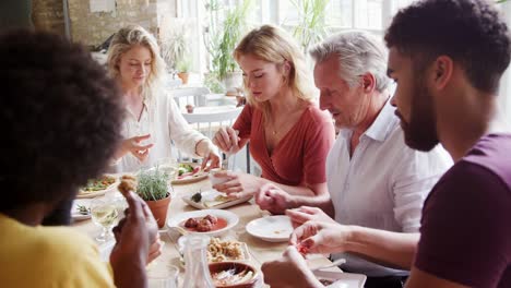 A-multi-ethnic,-mixed-age-group-of-adult-friends-eating-tapas-together-at-a-table-in-a-restaurant,-close-up,-selective-focus