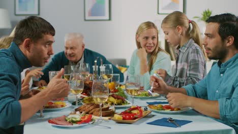 Große-Familie-und-Freunde-feiern-zu-Hause-versammelt-vielfältige-Gruppe-von-Kindern,-jungen-Erwachsenen-und-alten-Menschen-am-Tisch.-Essen,-Essen,-trinken-und-Spaß-Gespräch.-In-Zeitlupe.