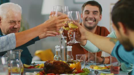 Familia-y-fiesta-de-amigos-en-casa,-grupo-diverso-de-niños,-jóvenes-y-viejas-personas-se-reunieron-en-la-mesa-tienen-divertida-conversación.-Tintineo-de-vasos-y-haciendo-tostadas.-En-cámara-lenta.