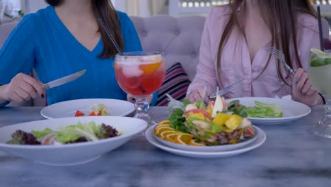 dieta-saludable,-las-mujeres-jóvenes-durante-una-cena-comunican-sentados-en-la-mesa-y-comer-ensalada-griega-en-café