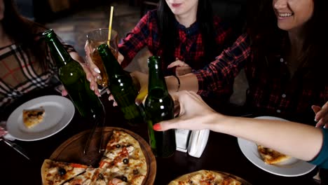 The-company-of-beautiful-girls-in-the-pizzeria-clinking-bottles-of-beer,-Close-up.