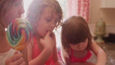 A-little-girl-eating-a-lollypop-and-then-eating-cookie-dough-with-her-sisters