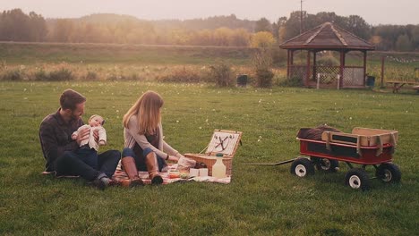 Un-Pareja-joven-en-un-picnic-con-su-bebé-en-un-día-de-otoño,-gran-angular-con-resplandor-del-objetivo