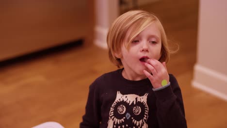 Little-girl-in-a-kitchen-with-ice-in-her-mouth,-and-a-boy-rides-by-on-a-scooter