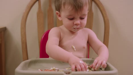 An-adorable-little-boy-in-a-high-chair-booster-seat-eating-messy-food-with-his-hands