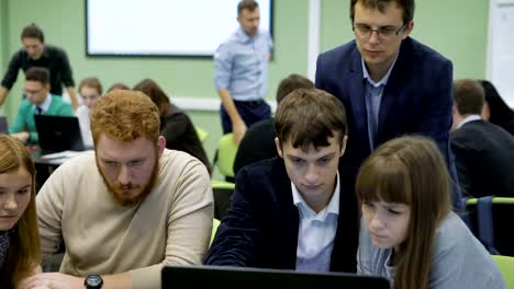 Close-up-of-business-team-preparing-the-presentation-of-their-startup.-Red-haired,-dark-haired-men-and-two-fair-haired-girls-dressed-in-casual-clothes-are-sitting-at-the-desk