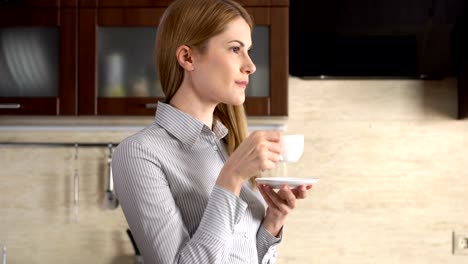 Beautiful-businesswoman-standing-in-her-kitchen-smiling.-Happy-and-relaxed-at-home.-Drinking-coffee