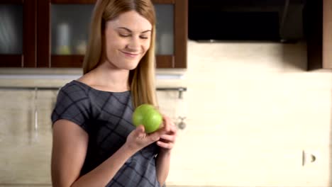 Beautiful-attractive-young-woman-with-green-apple-standing-in-her-kitchen.-Happy-and-relaxed-at-home