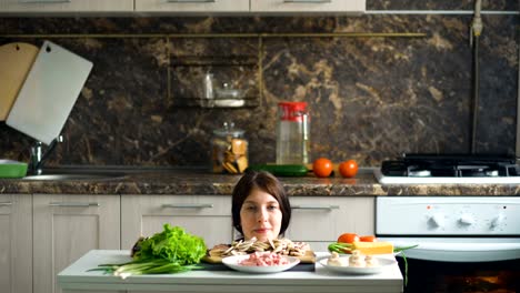 Portrait-of-beautiful-smiling-woman-cook-show-above-the-table-with-vegetables-in-kitchen-at-home