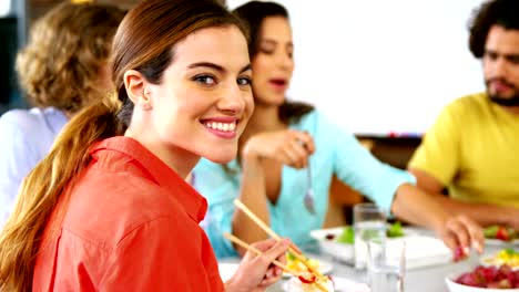 Portrait-of-woman-having-lunch-while-colleague-interacting-in-background