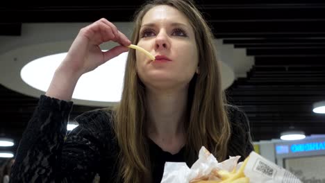 Mujer-joven-comiendo-hamburguesas-y-patatas-fritas