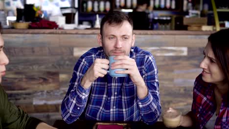 Interesting-appearance,-an-adult-man-enjoys-coffee,-which-is-poured-into-a-blue-cup,-not-paying-attention-to-the-two-girls-who-are-chatting-in-the-foreground