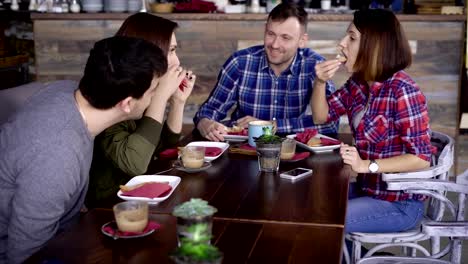 Una-empresa-adulta-de-amigos-come-deliciosos-sándwiches-con-pescado-y-verduras,-beber-café-con-leche-y-canela.-Las-personas-de-comunicarse,-divertirse-y-pasar-un-buen-rato-en-un-restaurante-acogedor