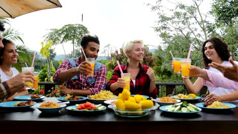 Leute-Toasten-Saft-Gläser-am-Tisch-sitzen-auf-der-Terrasse-essen-junge-Freunde-reden-im-freien-Kommunikation