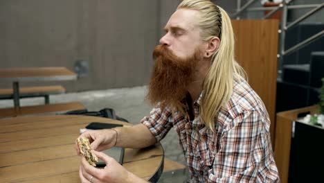 Bearded-student-man-eating-burger-in-street-cafe-outdoors