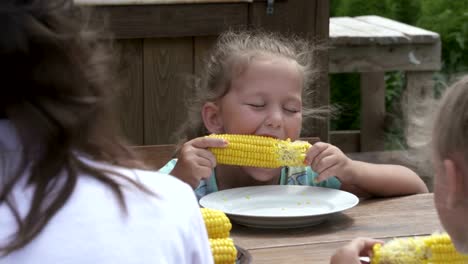 Niña-come-maíz-en-la-mazorca-en-la-mesa-de-comedor-al-aire-libre