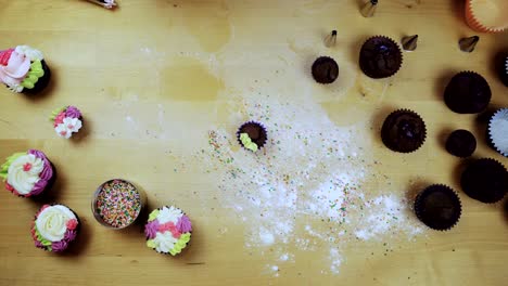 Top-view-of-chocolate-cupcakes-on-the-table.-Young-woman-decorating-muffins-with-colored-cream-from-pastry-bag