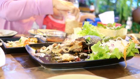 Mano-sacando-comida-de-pescado-ensalada-en-la-mesa-con-la-familia