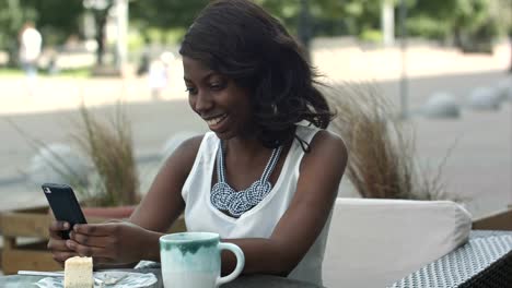 African-american-woman-using-phone,-while-sitting-in-outside-cafe