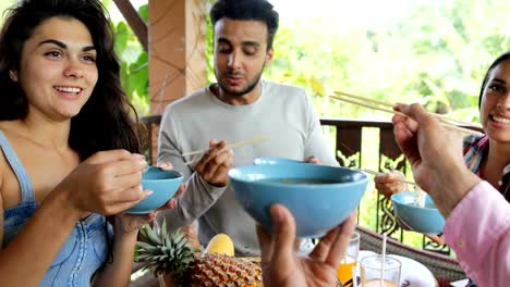 Personas-alimentadas-mutuamente-con-deliciosos-fideos-asiáticos-alimentos,-grupo-de-amigos-sentarse-en-la-mesa-en-terraza-vista-en-Bosque-Tropical