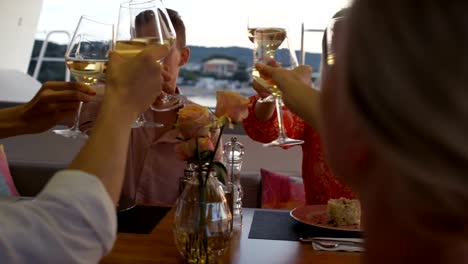 Gruppe-von-erfolgreichen-jungen-Menschen-essen-Wüsten-auf-Yacht.-Es-ist-Abend,-Meer-ist-ruhig-und-Inseln-sind-sichtbar-am-Horizont.