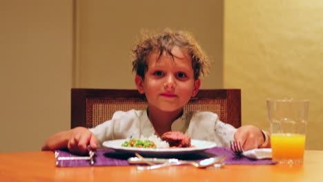 Niño-esperando-comida-llegar-a-la-mesa-en-4K-niño-joven-con-tenedor-y-cuchillo-en-la-mesa-pidiendo-comida-riendo-y-sonriendo-a-la-cámara-en-4K