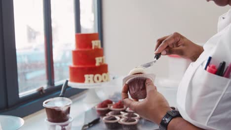 Female-baker-frosting-muffin-at-a-bakery,-mid-section