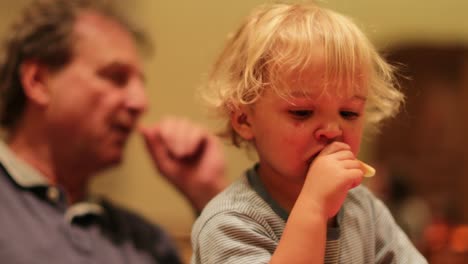 Candid-moment-of-baby-boy-eating-fruit-while-grand-father-is-seen-in-the-background.-Two-year-old-baby-eating-nutritious-food