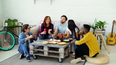 Amigos-felices-comiendo-pizza-y-celebrar-fiesta-tintineantes-botellas-con-cerveza-y-soda-sentado-en-el-sofá-en-casa