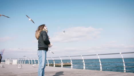 Young-woman-feeding-seagulls-at-winter-near-the-sea,-slow-motion