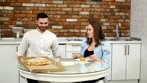 Man-and-pregnant-woman-eating-pizza-at-home-in-their-kitchen.-Poor-diet.-Fatty-foods.-Obesity