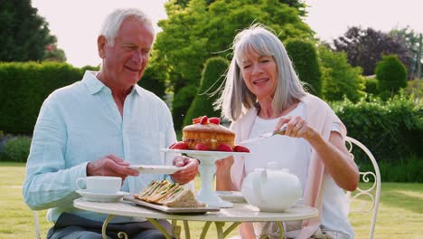 Retired-Couple-Enjoying-Afternoon-Tea-In-Garden-At-Home