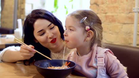 Joven-madre,-alimentan-a-su-pequeña-hija-con-una-tallarines-coreanos-en-restaurante